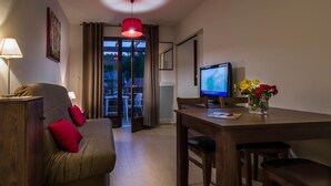 A room with a sofa, a dining table, a TV, and a view through a glass door. - Stay Near Prehistoric Sites (Les Eyzies)