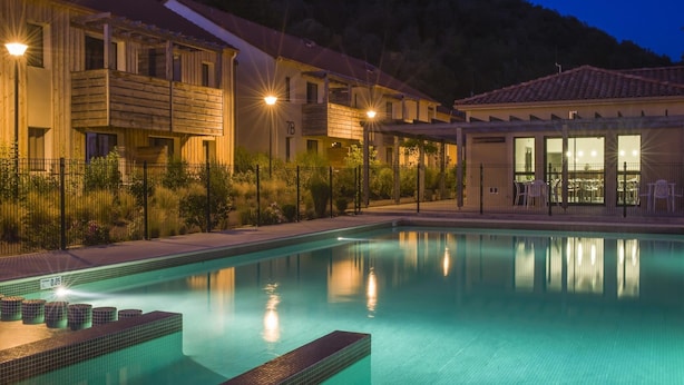 A swimming pool with a tiled deck, a building with a number '7B' sign, and a mountain backdrop. - Stay Near Prehistoric Sites (Les Eyzies)
