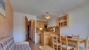 A cozy living area with a plaid sofa, wooden dining table, and chairs, a kitchen with wooden cabinets and a microwave, and a ceiling fan. - Bright Apartment Close to Ski-slopes (Les Deux Alpes)