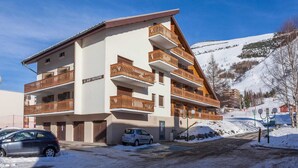 A multi-story hotel with balconies, a snow-covered parking area, and a mountainous backdrop. - Bright Apartment Close to Ski-slopes (Les Deux Alpes)