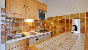 A kitchen with wooden cabinets, a microwave, a coffee maker, and a tiled backsplash. - Bright Apartment Close to Ski-slopes (Les Deux Alpes)