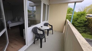 A balcony with a table and two chairs, a sliding glass door leading to a room with a bed and a window, and a view of greenery. - Baltic Sea vacation apartment K105 (Schönberg)