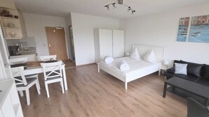 A modern, well-lit room with a bed, a black sofa, a dining table with chairs, and a kitchen area. - Baltic Sea vacation apartment K105 (Schönberg)