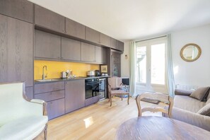 A modern kitchen with built-in appliances, a dining area with a wooden table and chairs, and a living room with a sofa and a chair. - Close to the Castle- Soothing and calm garden view (Versailles)
