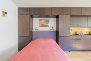 A bedroom with a bed, a small desk, and a kitchenette area. - Close to the Castle- Soothing and calm garden view (Versailles)