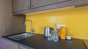 Une cuisine dotée d’un robinet moderne, d’une bouilloire, d’une cafetière et d’un dosseret de crédence recouvert de carreaux jaunes.