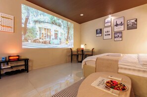 A hotel room with a bed, a small table with a remote control, a projection screen displaying a coffee shop, and framed pictures on the wall. - Le Places Old Condos Central Nguyen Hue  (Ho Chi Minh City)