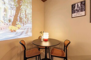 Una habitación con una mesa redonda, dos sillas de mimbre, un florero con utensilios y un cuadro enmarcado en la pared.