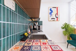 Una cocina con azulejos verdes, un lavamanos, un microondas y una alfombra colorida.