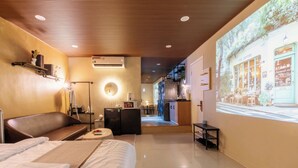 Ein Hotelzimmer mit Bett, einer Sitzecke, einer Küchenzeile und einer Projektion eines Cafés an der Wand.