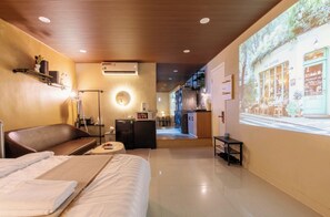 A hotel room with a bed, a seating area, a kitchenette, and a projection of a coffee shop on the wall. - Le Places Old Condos Central Nguyen Hue  (Ho Chi Minh City)