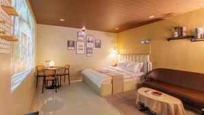 Een hotelkamer met een bed, een bank, een eettafel met stoelen, een projectiescherm en fotolijsten aan de muur.