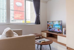 Una sala de estar moderna con sofá, mesa de centro, televisor y ventana con cortinas.