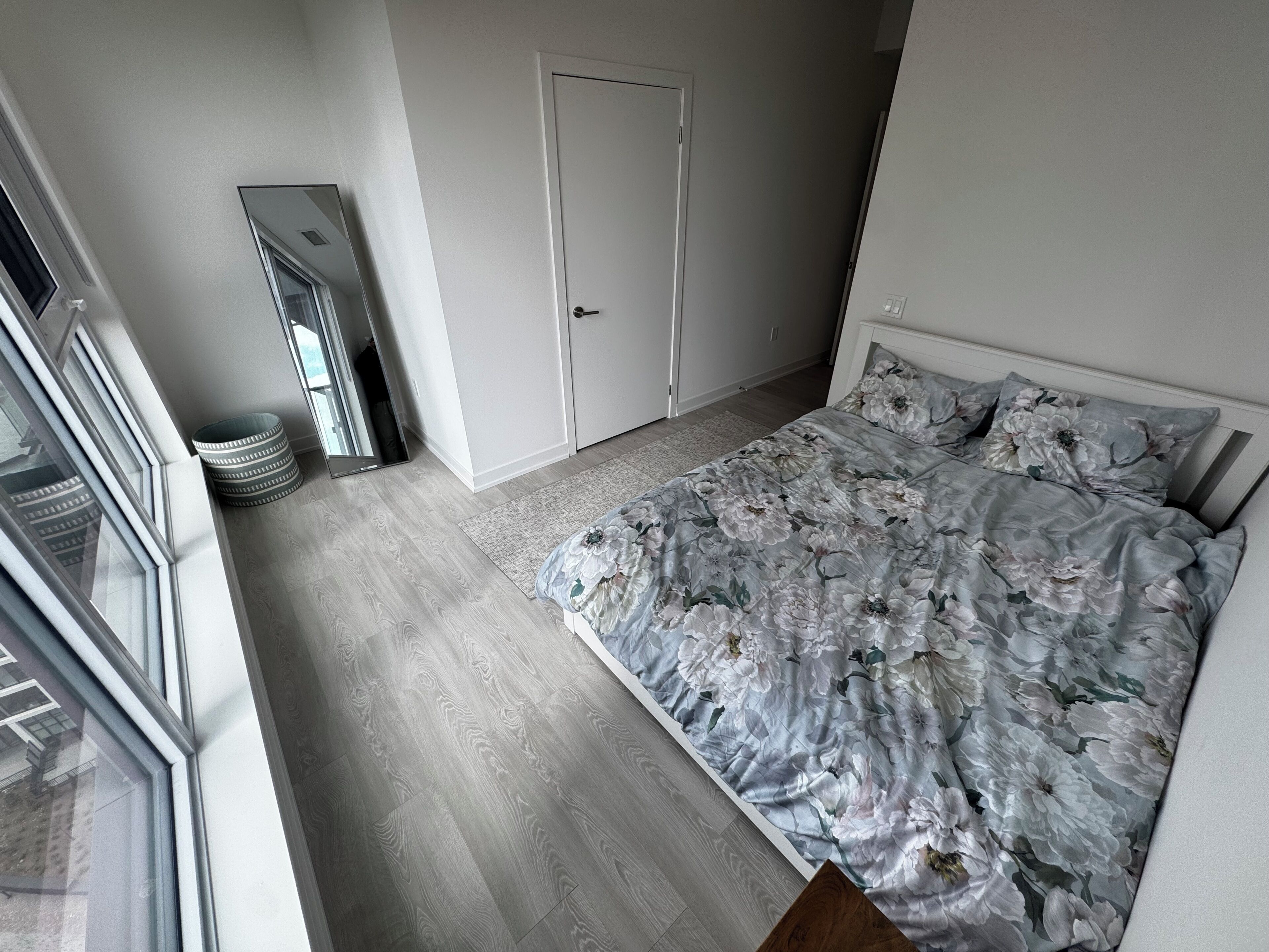 Quarto com cama, porta, espelho e janela.