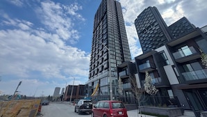En moderne bygate med høye bygninger, klar himmel og en rød bil parkert langs veien.