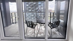 En balkon med et bord og stole, udsigt til en skyskraber og et bybillede.