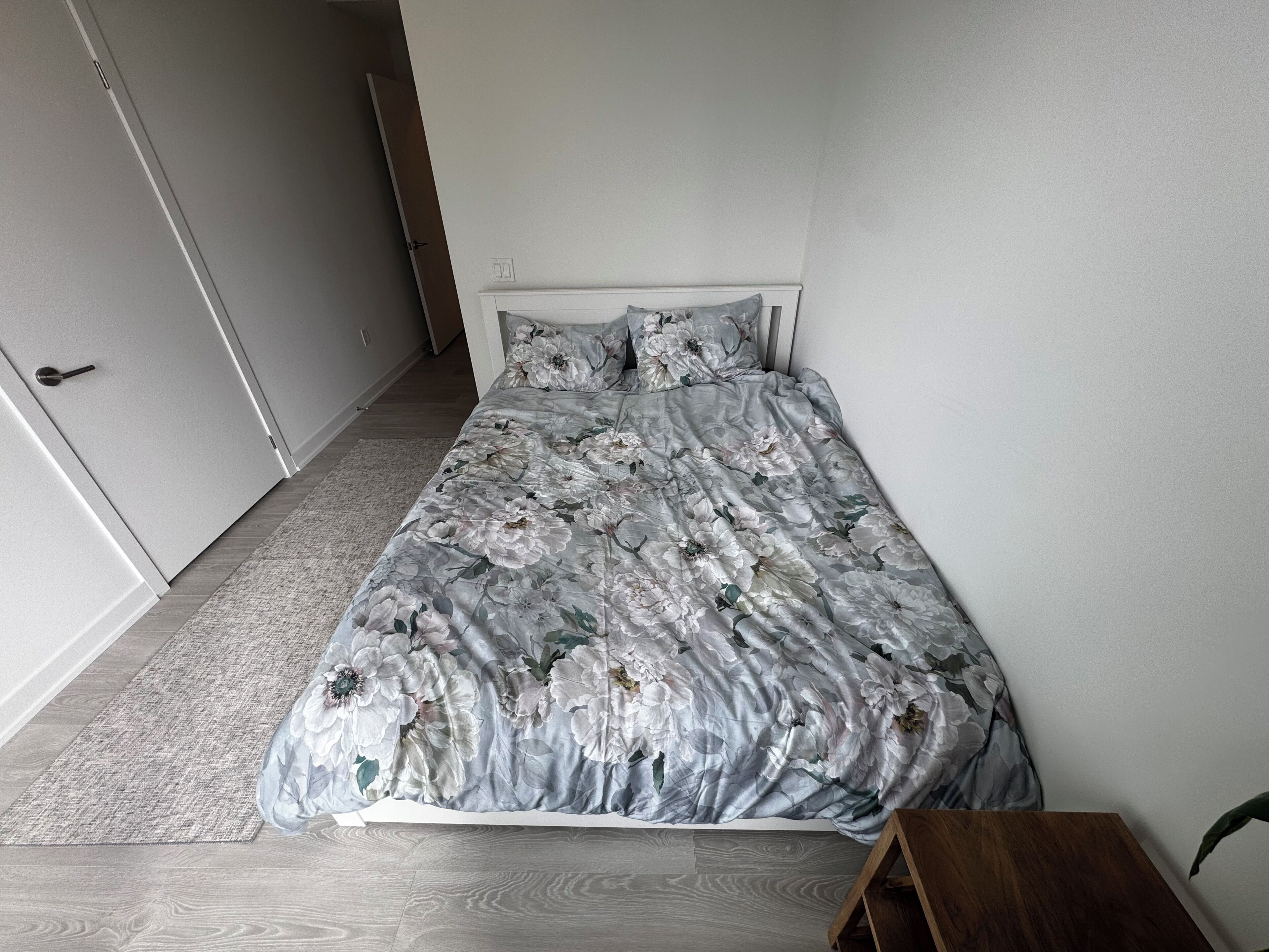 Une chambre à coucher avec un lit, un plancher en bois, une porte blanche et une petite table en bois.