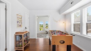 Ein Zimmer mit Kicker, einer Vitrine und einer Tür zum Balkon, sowie einem Fenster mit Jalousien.
