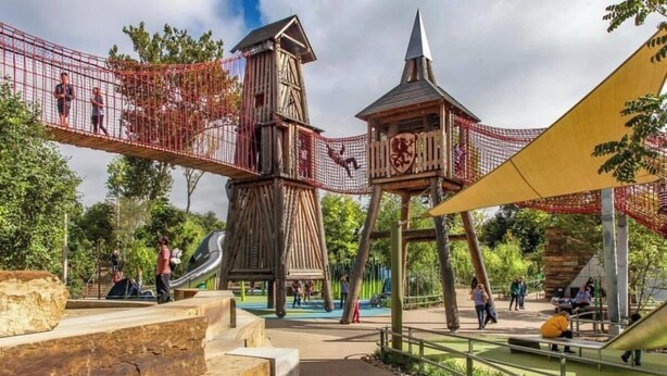 Een speeltuin met een touwbrug, een glijbaan en een houten toren.