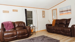Un salon avec deux canapés en cuir marron, un tapis gris, une petite table sur laquelle sont posés divers objets, et un tableau accroché au mur.