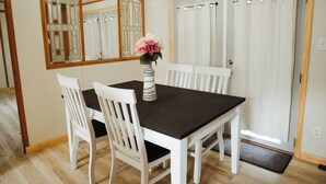 Un coin repas comprenant une table, des chaises, un vase avec des fleurs, un miroir et une porte avec des rideaux.
