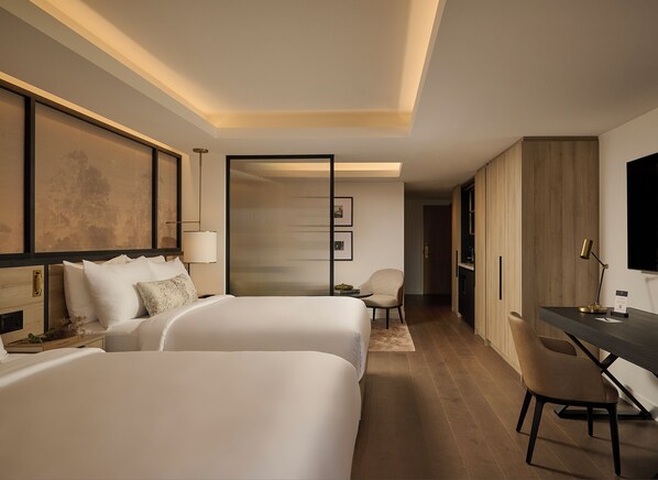 A hotel room with two beds, a desk, a chair, a television, and a sliding door leading to a bathroom.