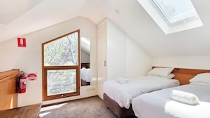 Een slaapkamer met twee bedden, een dakraam, een brandblusser en een raam met uitzicht op bomen.