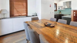 Een moderne keuken met witte kasten, een houten eettafel en grijze gestoffeerde stoelen.