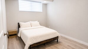 A bedroom with a bed, a window, and a wooden nightstand.