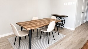 A dining area with a wooden table, four chairs, a small side table, and a patterned rug.