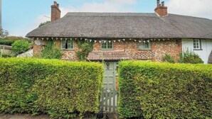 Une maison traditionnelle en briques, avec un toit de chaume, une porte verte et une clôture blanche.