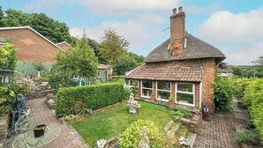 Une maison en briques avec un toit de chaume, un jardin agrémenté d’une fontaine et un chemin pavé.