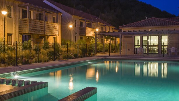 Una piscina con bordo piastrellato, un edificio con il cartello '7B' e montagne sullo sfondo.