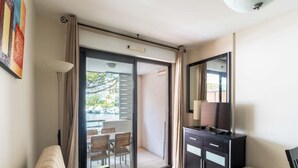 Ein Hotelzimmer mit Sofa, kleinem Tisch, Schrank, Fernseher und einer Glastür zum Außenbereich mit Stühlen und Blick aufs Wasser.