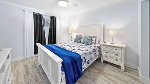 A bedroom with a white bed, a nightstand, a ceiling fan, and a window with curtains. - Cozy updated 2-bedroom condo with AC in serene Destin. (Destin)