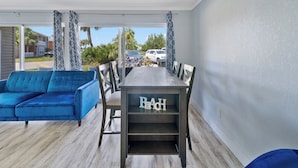 A dining area with a table and chairs, a blue sofa, and a view of the street and parked cars. - Cozy updated 2-bedroom condo with AC in serene Destin. (Destin)