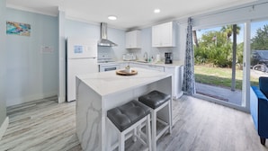 A modern kitchen with white cabinetry, a central island, and a view of the outdoors. - Cozy updated 2-bedroom condo with AC in serene Destin. (Destin)