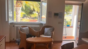 Ein Zimmer mit einem Korbstuhl-Tisch und -Stühlen, einem Heizkörper, einem Fenster mit Blick auf Palmen und einer Tür, die nach draußen führt.