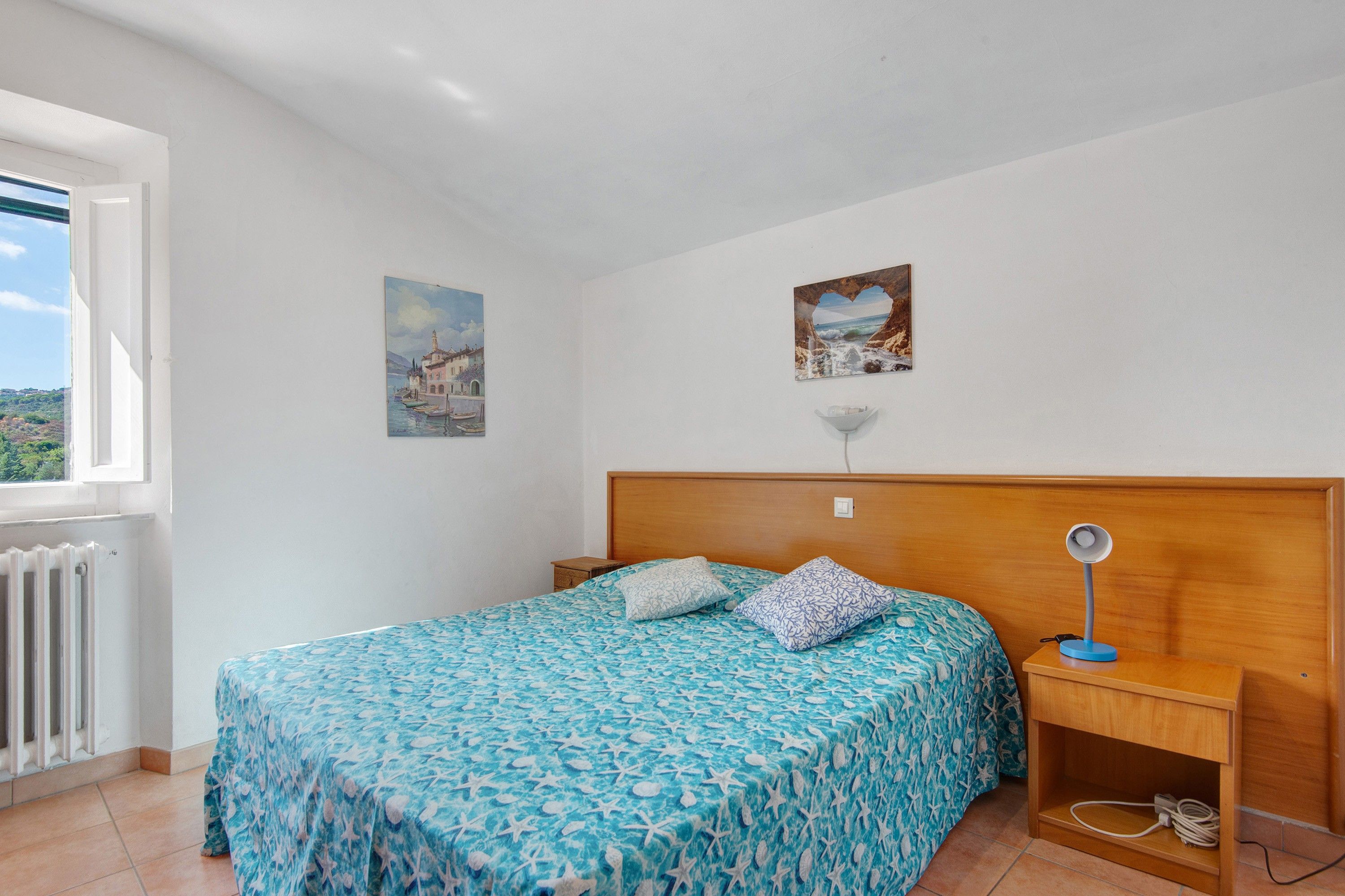 Ein Schlafzimmer mit einem Bett, einem Nachttisch, einer Lampe und zwei Bildern an der Wand.