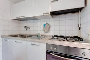 A kitchen with white cabinets, a stainless steel sink, a gas stove, and a built-in oven. - Apartment 'Agave' with Private Garden, Wi-Fi and Air Conditioning (Marina di Campo)