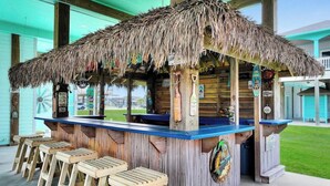 Un bar de style tiki avec un toit de chaume, des tabourets en bois et un comptoir bleu.