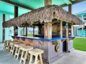 A tiki bar with a thatched roof, wooden stools, and a blue counter. - On Beach Time*Prime Location (Bolivar Peninsula)