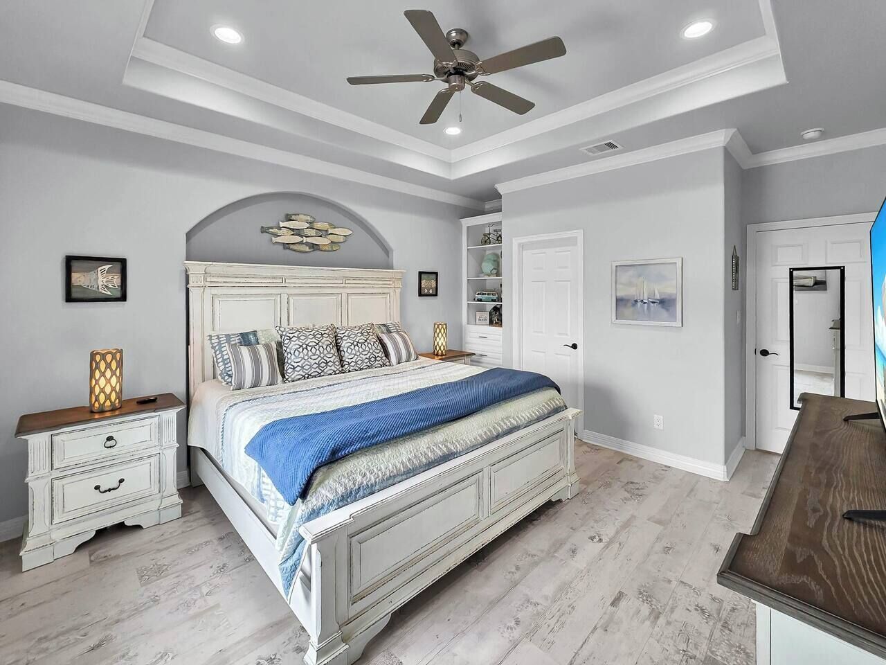 Une chambre à coucher avec un lit, des tables de chevet, un ventilateur de plafond et une porte.