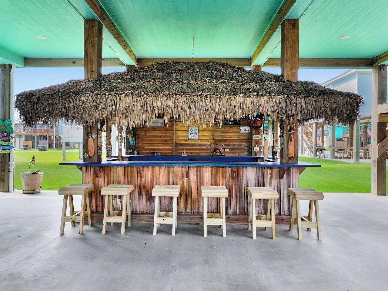 A tiki bar with a thatched roof, wooden stools, and a blue bar counter.