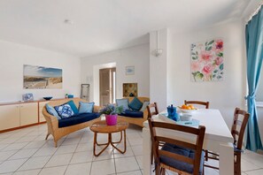 A modern living room with a sofa, dining table, and chairs. There is a potted plant on the table.