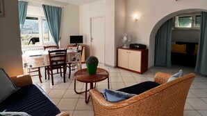 Una sala de estar con muebles de mimbre, un comedor con una mesa y sillas, y una cocina con un armario y un ventilador.