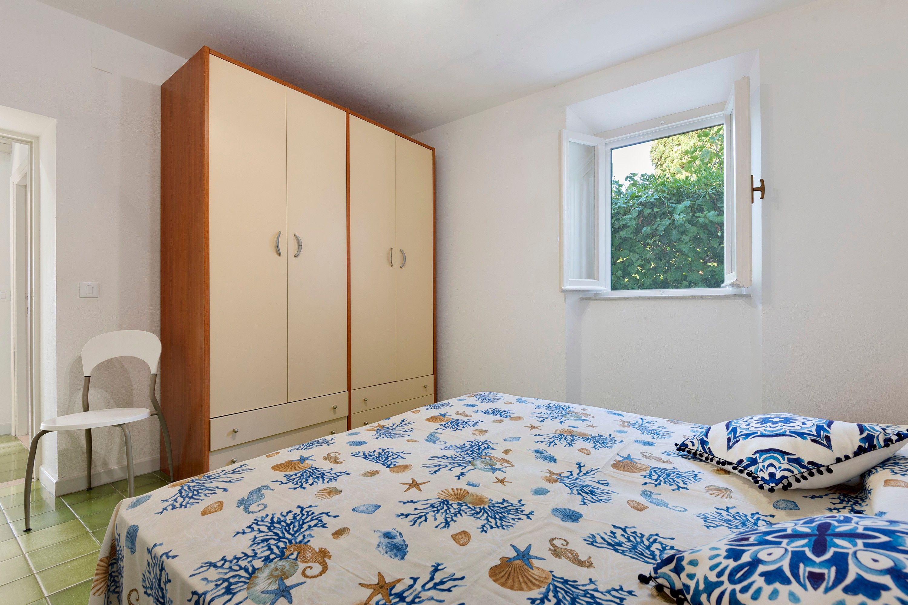 Una camera da letto con un letto, un armadio, una sedia e una finestra vista verde.