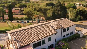 Un edificio de dos plantas con tejado de baldosas, rodeado de vegetación y vistas despejadas al mar.