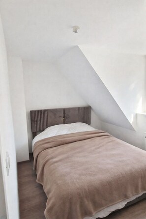A bedroom with a sloped ceiling, a bed with a headboard, and a brown blanket. - Duplex luxueux de 130 m2 Centre-ville et plage à 400 m (Le Portel)