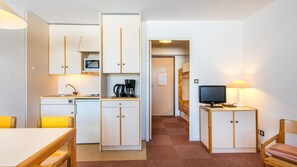 Una habitación de hotel compacta con kitchenette, zona de comedor, televisor y un pequeño rincón de estar.